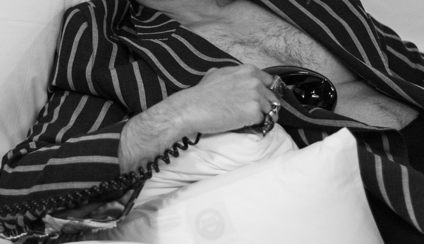 A hand with rings holding a telephone receiver, the coiled cord running across white linen